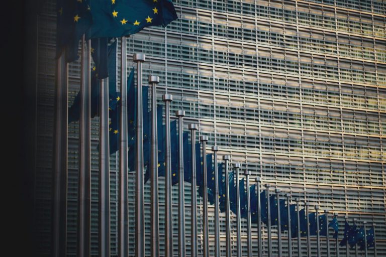 Row of European Union flags outside a modern glass building