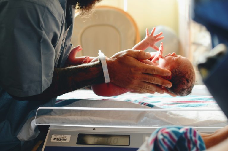 Newborn being held by a caregiver in a hospital bassinet