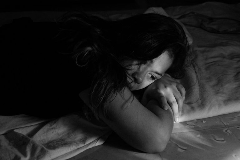 Woman lying on a bed with her head resting on her arm in dim light