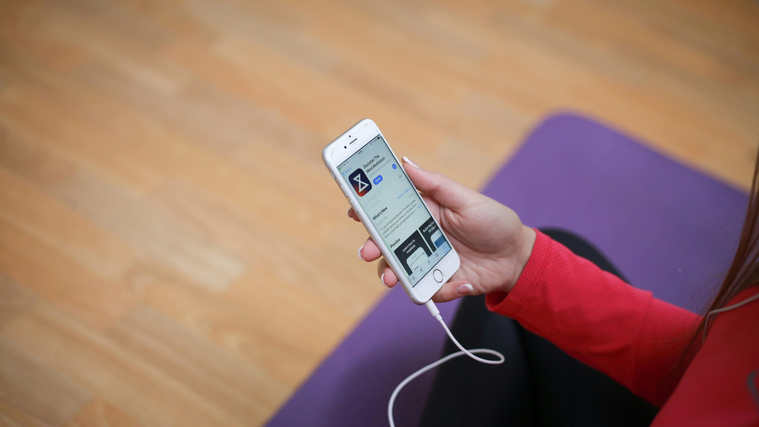 Person holding a smartphone with a meditation app open while sitting on a yoga mat