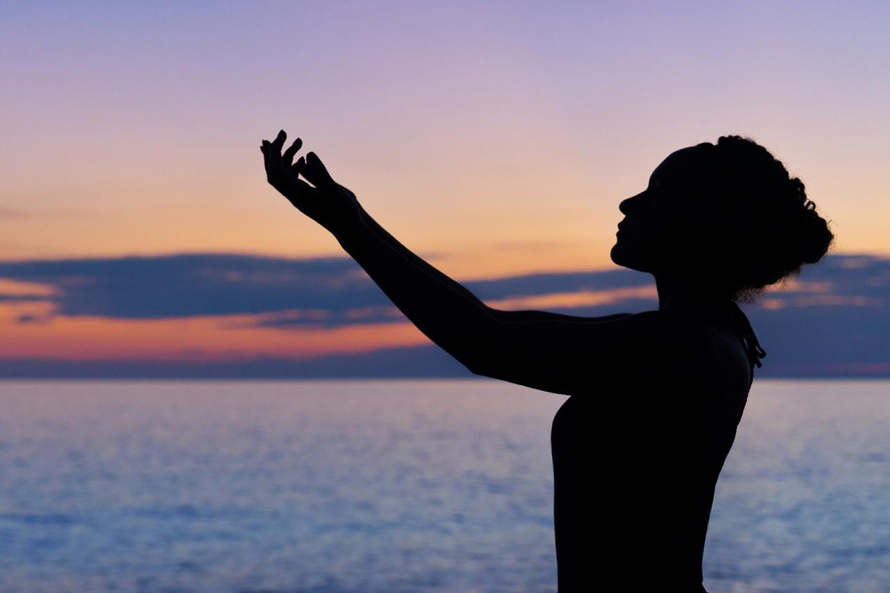 Silhouette of a woman with raised arms at the beach during sunset